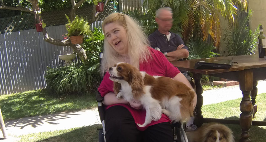 Ann Marie Smith Photo of Ann Marie Smith in a garden. She has a big smile, long light blonde hair down to her shoulders, wears a red top and has a dog in her lap.