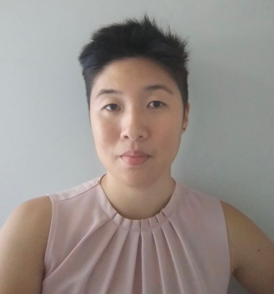 Photo of Isabel against a grey backdrop. She is an Asian woman with black short cropped hair, and wears a pink sleeveless top.