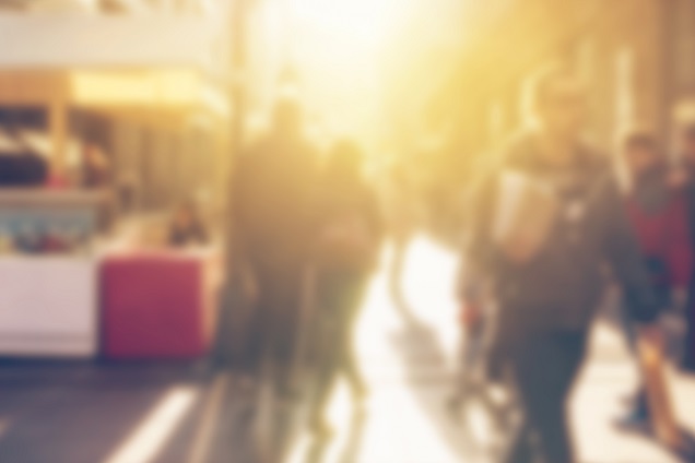 Blurred photo of people walking on a street on a sunny day.