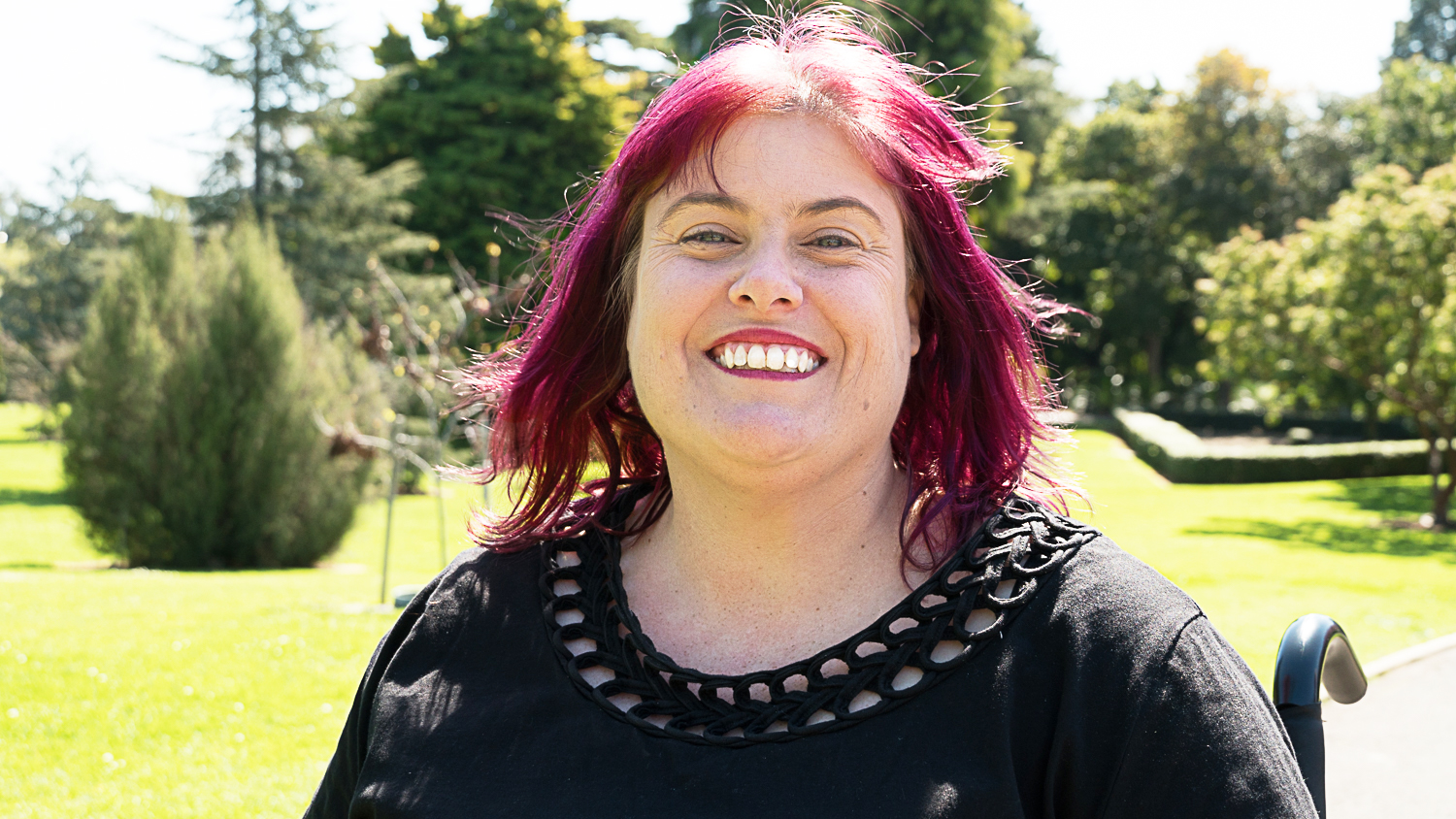 Photo of Christine Priest Photo of Christine Priest outside with a huge smile and purple hair