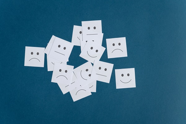 Dark teal background with white Post-it notes that have faces on them. The faces show a smiling, neutral or sad expression.