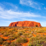 Photo of uluru against a blue, lightly cloudy sky