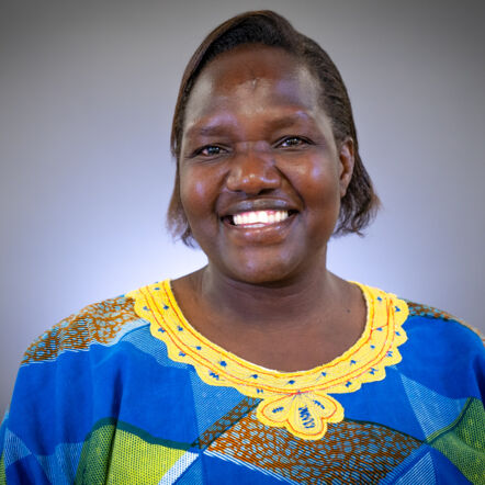 Photo shows Esther against a grey backdrop. She is African, with short chin length dark hair and a big smile.