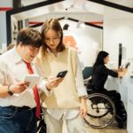 2 people, one with a visible disability, looking at something on a mobile phone screen.