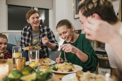 Photo of a group of people having a meal together. Photo shows a group of 2 men an 2 women at a table enjoying a meal together at home.