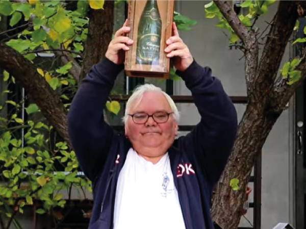 Image is Collin holding the champagne bottle trophy over his head in victory.