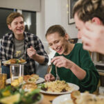 Photo shows a group of 2 men an 2 women at a table enjoying a meal together at home.