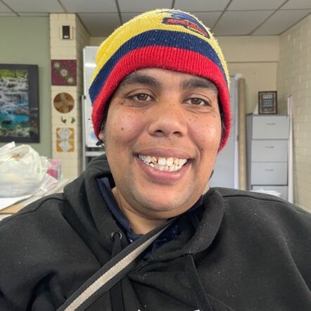 Photo of Carissa flashing a big smile at the camera. She is an Aboriginal woman wearing an Adelaide Crows beanie and black jumper.