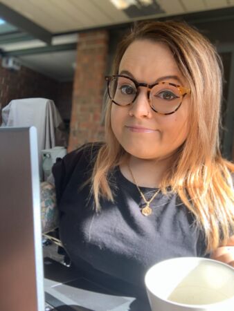 Belle working from home. She has tortoiseshell glasses on and a cup next to her laptop.