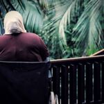 Photo of a lonely wheelchair user wearing a yellow headscarf on a outdoor balcony.